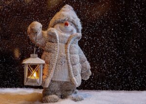 Schneemann im Schnee mit brennender Kerze in der Laterne
