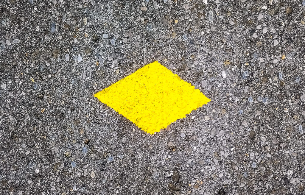 Schweizer Wanderwege Gelbes Wanderzeichen auf Asphalt